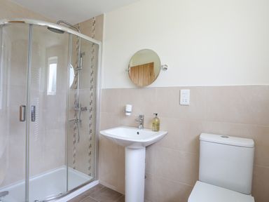 A bathroom with a glass shower enclosure a white pedestal sink with soap dispenser a round mirror and a toilet at The Piggery in LLanfair Talhaiarn near Abergele