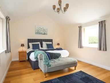 A bedroom with a double bed two bedside tables with lamps a chaise lounge and two windows at The Piggery in LLanfair Talhaiarn near Abergele
