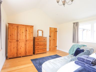 A bedroom with wooden wardrobe and chest of drawers next to a wooden door and window with curtains at The Piggery in LLanfair Talhaiarn near Abergele