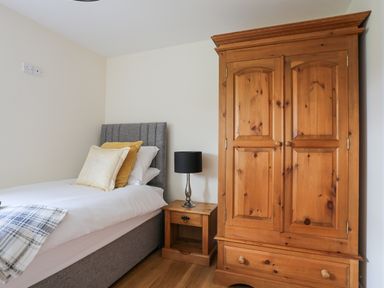 A bedroom with a single bed, bedside table with lamp, and wooden wardrobe at The Piggery in LLanfair Talhaiarn near Abergele