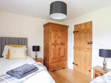 A bedroom with a gray bed headboard pillows wooden wardrobe lamps and wooden door at The Piggery in LLanfair Talhaiarn near Abergele