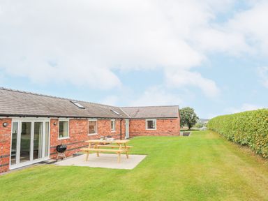 A red brick house with a patio table and barbecue grill on a lawn at The Piggery in LLanfair Talhaiarn near Abergele