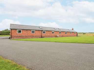 A long single-story brick building with multiple windows and skylights with a paved driveway and grassy lawn