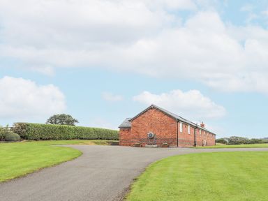 A paved driveway leading to a long brick building surrounded by grass and hedges at The Piggery in LLanfair Talhaiarn near Abergele