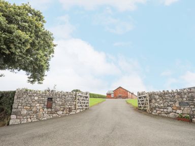 A driveway with stone walls and wooden gates leading to a brick building at The Piggery in LLanfair Talhaiarn near Abergele