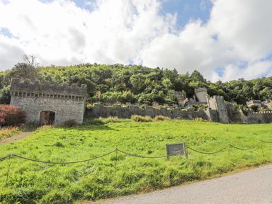 A stone castle wall with turrets and flags on a grassy hill under a partly cloudy sky