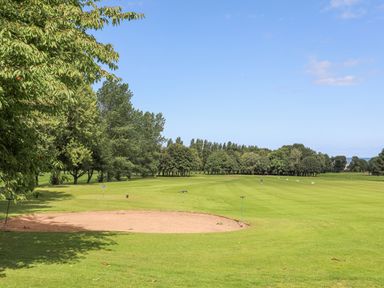 A golf course with a sand bunker and trees in the background at The Piggery in LLanfair Talhaiarn near Abergele