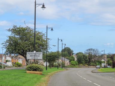 A road with street lamps and a sign for Abergele near houses and trees at The Piggery in LLanfair Talhaiarn near Abergele
