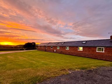 A long single-story brick building with windows and skylights next to a grassy area at sunset at The Piggery in LLanfair Talhaiarn near Abergele