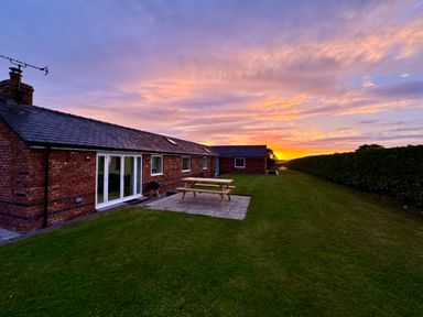 A brick house with a slate roof patio table and grill on grass at The Piggery in LLanfair Talhaiarn near Abergele