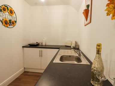 A small kitchen area with a sink toaster kettle and a bottle of champagne at Bee Cottage in Ottinge near Lyminge