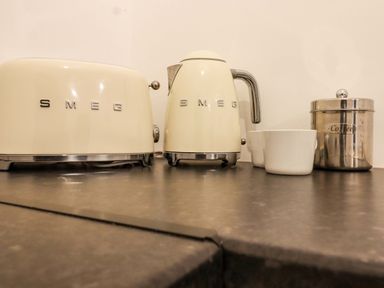 A kitchen countertop with a cream SMEG toaster, SMEG kettle, two white cups, and a stainless steel coffee container at Bee Cottage in Ottinge near Lyminge