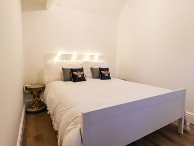A bedroom with a white bed and pillows with bee designs and a rustic bedside table at Bee Cottage in Ottinge near Lyminge
