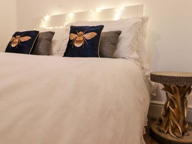 A bedroom with a white bed and pillows with bee designs next to a wooden side table at Bee Cottage in Ottinge near Lyminge