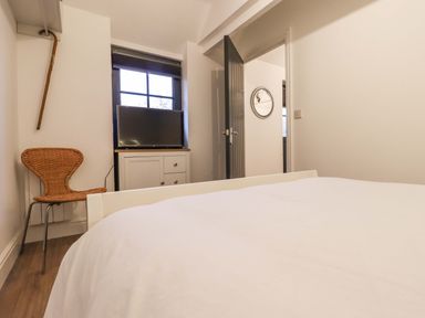 A bedroom with a bed a wicker chair a cabinet with a television and an open door at Bee Cottage Ottinge near Lyminge