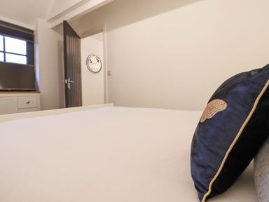A bedroom with a bed and pillow a cabinet with a television and an open door showing a round mirror at Bee Cottage in Ottinge near Lyminge