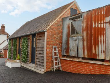 A small brick and wood building with a corrugated metal section and a ladder outside at Bee Cottage in Ottinge near Lyminge