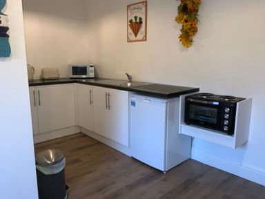 A kitchen with white cabinets a microwave a toaster a kettle a small fridge a sink and a small oven with stove at Bee Cottage in Ottinge near Lyminge