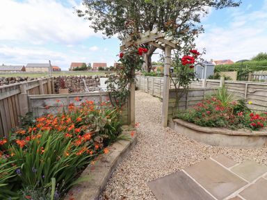 A garden with a pathway and flowers at Lavender Cottage Beadnell