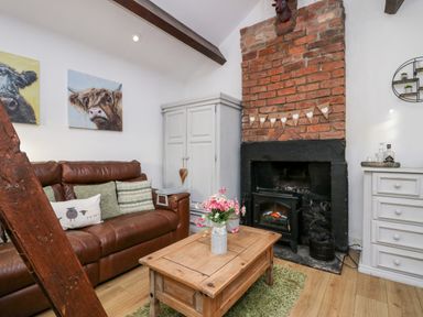 A living room with a brown leather sofa cushions a wooden coffee table a brick fireplace and white furniture at High Wreah Bolt Hole in Cleator Moor