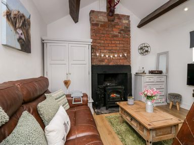 A living room with a leather sofa wooden coffee table a brick fireplace and white cabinets at High Wreah Bolt Hole in Cleator Moor