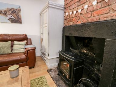A living room with a brown leather sofa green cushions a white cabinet a black stove in a fireplace and a cow painting on the wall at High Wreah Bolt Hole in Cleator Moor