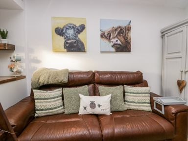 A brown leather sofa with five cushions and two paintings of cows on the wall at High Wreah Bolt Hole in Cleator Moor