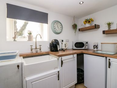 A kitchen with a sink wooden countertops a microwave kettle an air fryer and shelves with flowers at High Wreah Bolt Hole in Cleator Moor