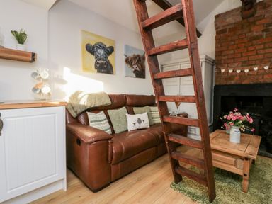 A living room with a brown leather sofa and wooden ladder next to a brick fireplace at High Wreah Bolt Hole in Cleator Moor