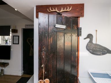 A rustic wooden door with a bathroom sign and antlers above it in a room with a duck-shaped chalkboard on the wall at High Wreah Bolt Hole in Cleator Moor