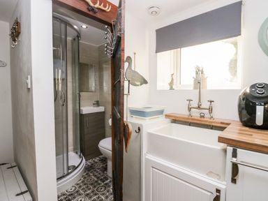 A small bathroom with a shower, toilet, sink, and a utility sink with a faucet under a window at High Wreah Bolt Hole in Cleator Moor