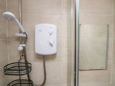 A shower area with a showerhead water heater and a small mirror at High Wreah Bolt Hole in Cleator Moor