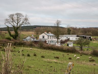 A rural farm with a white house surrounded by trees and fields with grazing sheep at High Wreah Bolt Hole in Cleator Moor