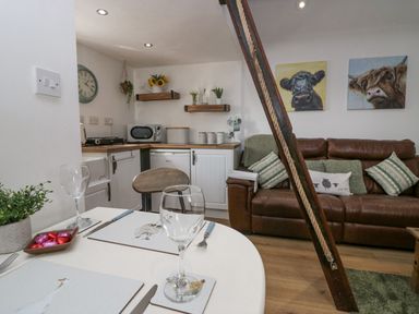 A small kitchen and living area with a brown leather sofa and dining table set at High Wreah Bolt Hole in Cleator Moor