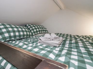 A bed with green and white checkered bedding and folded towels on top at High Wreah Bolt Hole in Cleator Moor