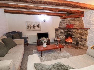 A living room with a stone fireplace a television a wooden coffee table with flowers and glasses and sofas at Ty Ceffylau in Llanllwni near Llanybydder