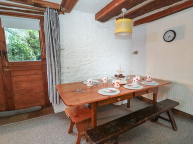 A dining area with a wooden table set with plates mugs and cutlery a bench and stools by a wooden door at Ty Ceffylau in Llanllwni near Llanybydder