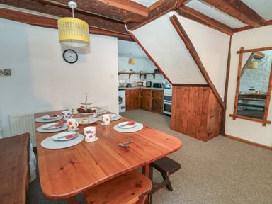 A dining area with a wooden table set for six and a small kitchen area with wooden cabinets at Ty Ceffylau in Llanllwni near Llanybydder
