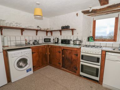 A kitchen with wooden cabinets washing machine microwave oven and window at Ty Ceffylau in Llanllwni near Llanybydder