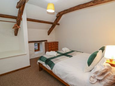 A bedroom with a double bed green and white pillows wooden dresser and exposed wooden ceiling beams at Ty Ceffylau in Llanllwni near Llanybydder