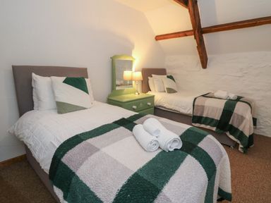 A bedroom with two single beds green and white cushions nightstand with a lamp and mirror at Ty Ceffylau Llanllwni near Llanybydder