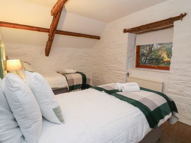 A bedroom with two single beds white bedding and checkered blankets a window and exposed wooden ceiling beams at Ty Ceffylau Llanllwni near Llanybydder