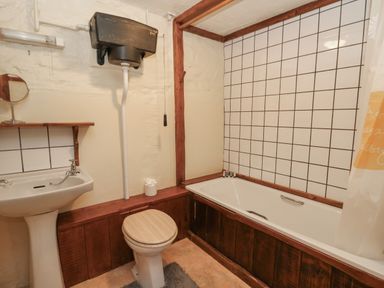 A bathroom with a pedestal sink a toilet with a wooden seat and a bathtub with tiled walls at Ty Ceffylau in Llanllwni near Llanybydder