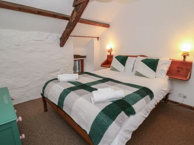 A bedroom with a double bed with green and white bedding and pillows with wooden wall shelves on each side at Ty Ceffylau in Llanllwni near Llanybydder