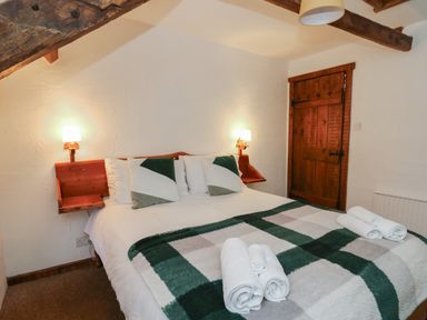 A bedroom with a double bed green and white pillows rolled towels on the blanket wooden door and two wall lamps at Ty Ceffylau in Llanllwni near Llanybydder