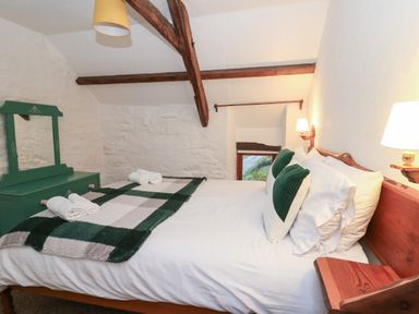 A bedroom with a bed with white sheets green pillows and a checkered blanket with a green dresser and mirror at Ty Ceffylau Llanllwni near Llanybydder