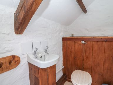 A small bathroom with a wooden toilet seat and a white sink with two taps at Ty Ceffylau in Llanllwni near Llanybydder