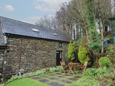 A stone building with two skylights and a door in a garden with a wooden table and chairs at Ty Ceffylau in Llanllwni near Llanybydder