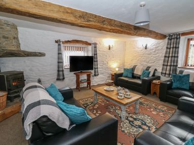 A living room with black leather sofas a wooden coffee table with tea set a patterned rug and a stone wall at Y Beudy in Cwmiar near Llanybydder