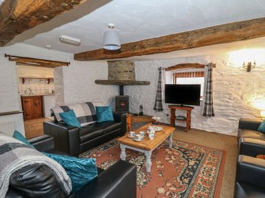 A living room with leather sofas a wooden coffee table a patterned rug and a wood stove at Y Beudy in Cwmiar near Llanybydder